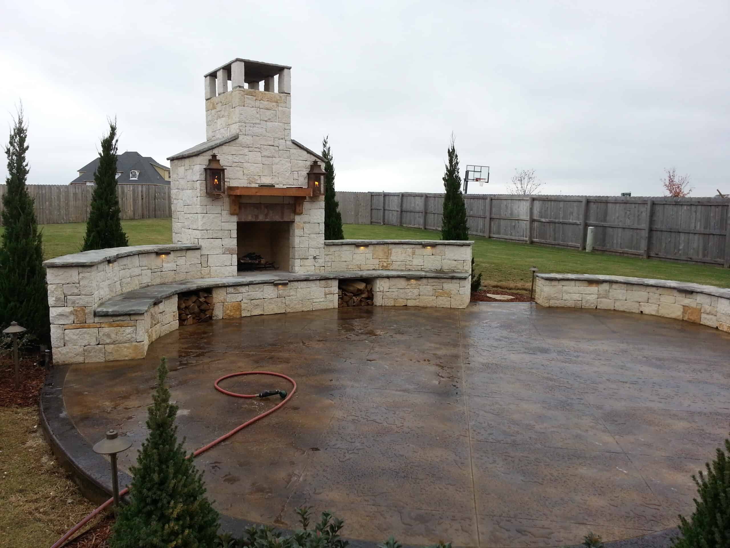 Outdoor stone fireplace and landscape design installation beside a residential property