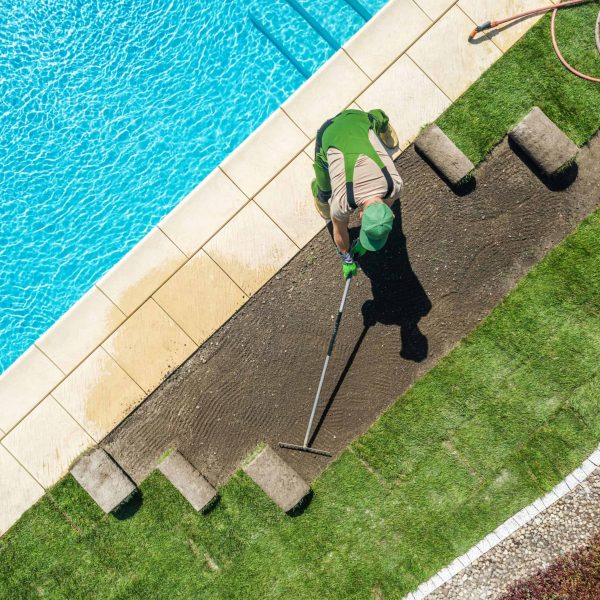 Landscaper installing artificial grass near a pool as part of a custom landscape design
